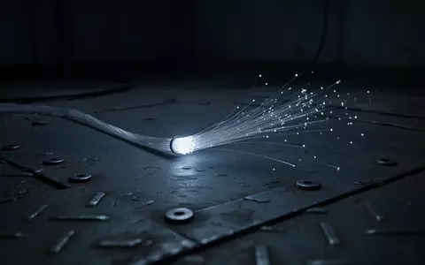Ein einzelnes leuchtendes Glasfaserkabel auf einer dunklen, industriellen Metalloberfläche bei gedimmtem Licht. - Foto: über boerse-global.de