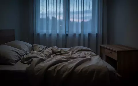 Ein ungemachtes Bett in einem ruhig beleuchteten Schlafzimmer bei Dämmerung, das eine Atmosphäre von Erschöpfung und Stille vermittelt. - Foto: über boerse-global.de