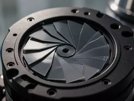 Nahaufnahme einer hochpräzisen mechanischen Blendenkonstruktion mit überlappenden Lamellen in einer Laborumgebung. - Foto: über boerse-global.de