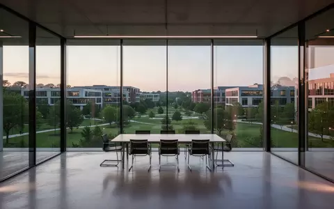 Ein leerer, moderner Konferenzraum mit Glaswänden und Blick auf einen weitläufigen Forschungscampus während der Dämmerung. - Foto: über boerse-global.de