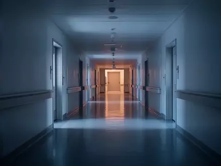 Ein ruhiger, leerer Krankenhausflur in gedämpftem blauem Licht mit klaren architektonischen Linien und ohne Personen. - Foto: über boerse-global.de