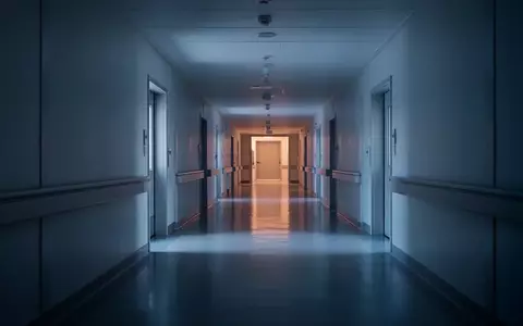 Ein ruhiger, leerer Krankenhausflur in gedämpftem blauem Licht mit klaren architektonischen Linien und ohne Personen. - Foto: über boerse-global.de