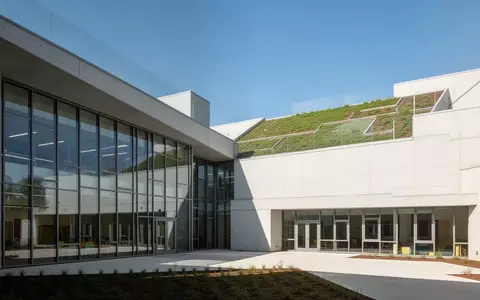 Moderner Schulneubau mit hellen Fassaden, großen Fensterflächen und begrüntem Dach bei Tageslicht. - Foto: über boerse-global.de