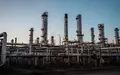 Industrielle Ölraffinerie bei Dämmerung mit komplexen Rohrleitungen und Destillationsanlagen vor einem klaren Abendhimmel. - Foto: über boerse-global.de