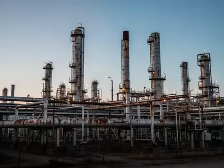 Industrielle Ölraffinerie bei Dämmerung mit komplexen Rohrleitungen und Destillationsanlagen vor einem klaren Abendhimmel. - Foto: über boerse-global.de