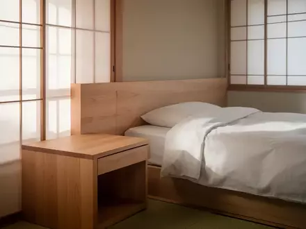Ein helles, minimalistisches Schlafzimmer mit einem Holznachttisch und weichem Tageslicht, das durch einen Sichtschutz fällt. - Foto: über boerse-global.de