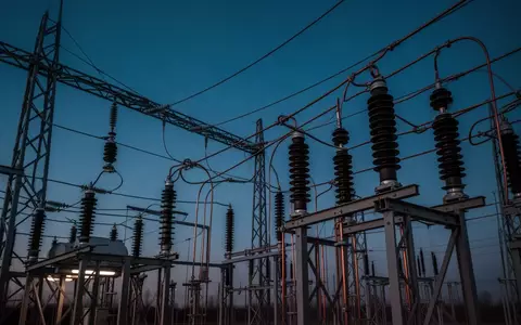 Eine industrielle Hochspannungsanlage bei Dämmerung mit komplexer Verkabelung und Metallstrukturen vor einem dunklen Himmel. - Foto: über boerse-global.de