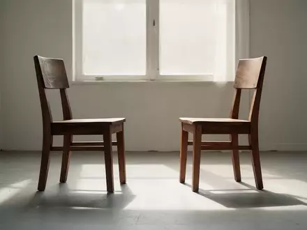Zwei leere Stühle, die einander in einem hellen, minimalistischen Raum gegenüberstehen und eine Atmosphäre zwischenmenschlicher Verbundenheit erzeugen. - Foto: über boerse-global.de