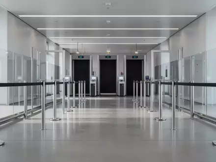 Ein leerer, minimalistischer Sicherheitsbereich an einem Flughafen mit Edelstahlpfosten und Glaswänden in ruhigem Licht. - Foto: über boerse-global.de