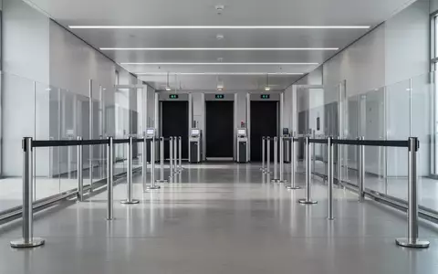 Ein leerer, minimalistischer Sicherheitsbereich an einem Flughafen mit Edelstahlpfosten und Glaswänden in ruhigem Licht. - Foto: über boerse-global.de