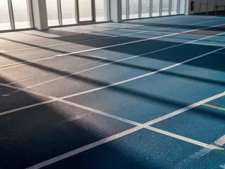 Eine leere, moderne Leichtathletikbahn in einer Sporthalle mit weichen Lichtverhältnissen und geometrischen Linien. - Foto: über boerse-global.de