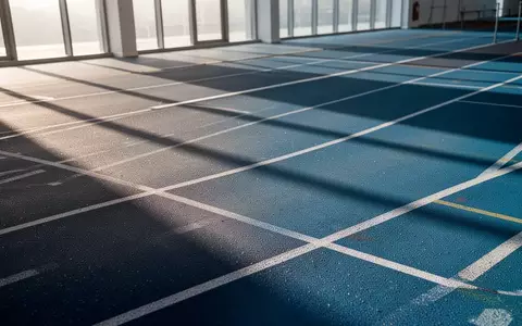 Eine leere, moderne Leichtathletikbahn in einer Sporthalle mit weichen Lichtverhältnissen und geometrischen Linien. - Foto: über boerse-global.de