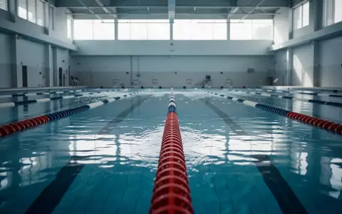Eine leere Schwimmbahn in einem Hallenbad mit klarem blauem Wasser und einer Bodenmarkierung. - Foto: über boerse-global.de