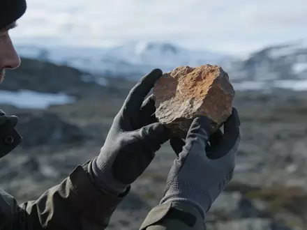 Geologe untersucht eine Gesteinsprobe in einer nordischen Landschaft. - Foto: über boerse-global.de