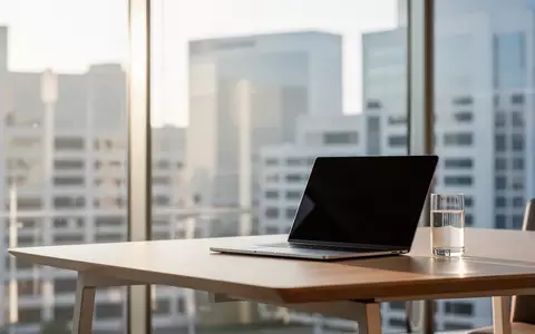 Ein heller, moderner Büroarbeitsplatz mit einem Laptop auf einem Schreibtisch vor einer großen Fensterfront. - Foto: über boerse-global.de