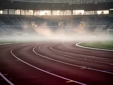 Eine leere, geschwungene Kunststoff-Laufbahn in einem Stadion bei Morgendämmerung und leichtem Nebel. - Foto: über boerse-global.de
