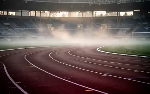 Eine leere, geschwungene Kunststoff-Laufbahn in einem Stadion bei Morgendämmerung und leichtem Nebel. - Foto: über boerse-global.de