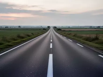 Eine leere, asphaltierte Landstraße in einer ruhigen Landschaft bei Dämmerung. - Foto: über boerse-global.de