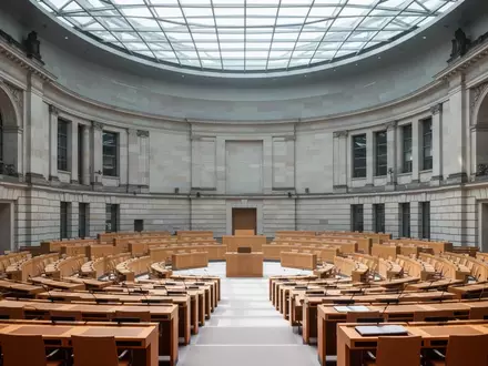 Leerer Plenarsaal des Deutschen Bundestages mit Fokus auf die Architektur und die hölzernen Sitzreihen. - Foto: über boerse-global.de