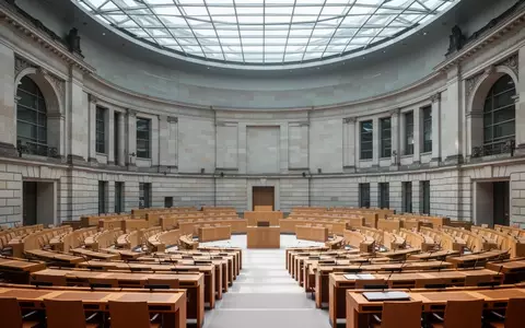 Leerer Plenarsaal des Deutschen Bundestages mit Fokus auf die Architektur und die hölzernen Sitzreihen. - Foto: über boerse-global.de