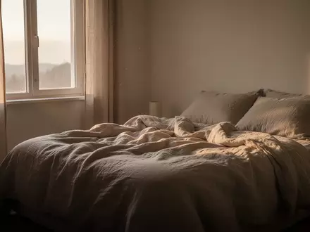 Ein minimalistisch eingerichtetes Schlafzimmer in den frühen Morgenstunden mit sanftem Tageslicht, das auf ein ungemachtes Bett fällt. - Foto: über boerse-global.de