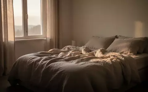 Ein minimalistisch eingerichtetes Schlafzimmer in den frühen Morgenstunden mit sanftem Tageslicht, das auf ein ungemachtes Bett fällt. - Foto: über boerse-global.de