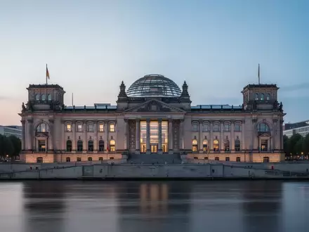Das Reichstagsgebäude in Berlin bei Dämmerung, aufgenommen von der Spree aus mit Fokus auf die Architektur. - Foto: über boerse-global.de