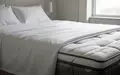Nahaufnahme der Textur hochwertiger, weißer Bettwäsche und einer Matratzenkante in einem hellen, minimalistischen Schlafzimmer. - Foto: über boerse-global.de