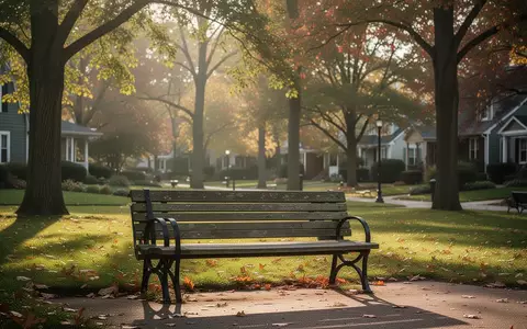 Eine leere Parkbank in einem sonnendurchfluteten, grünen Stadtpark im Herbst. - Foto: über boerse-global.de