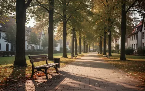 Ein sonniger Parkweg mit einer leeren Holzbank in einer kleinen Stadt, der Barrierefreiheit und öffentliche Räume symbolisiert. - Foto: über boerse-global.de