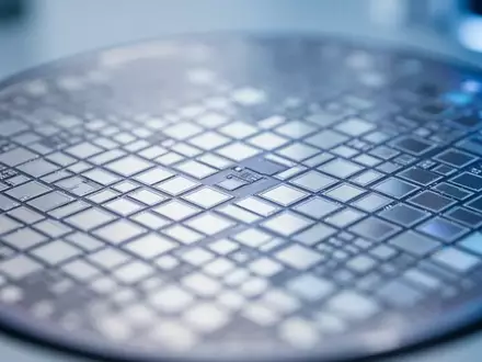 Nahaufnahme eines Silizium-Wafers mit einem präzisen Gitter aus mikroskopischen Spiegelstrukturen unter Laborlicht. - Foto: über boerse-global.de