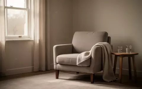 Ein ruhiger, minimalistisch eingerichteter Raum mit einem leeren Sessel und einer Decke, der eine Atmosphäre der Stille vermittelt. - Foto: über boerse-global.de
