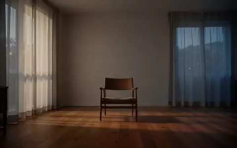 Ein minimalistisch eingerichteter, ruhiger Wohnraum mit einem leeren Sessel vor einer kahlen Wand bei Dämmerung. - Foto: über boerse-global.de