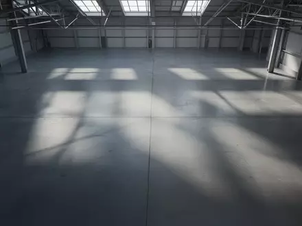 Leere, minimalistische Produktionshalle mit poliertem Betonboden und geometrischen Schattenwürfen durch einfallendes Tageslicht. - Foto: über boerse-global.de