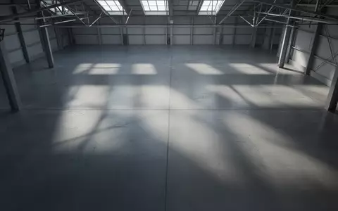 Leere, minimalistische Produktionshalle mit poliertem Betonboden und geometrischen Schattenwürfen durch einfallendes Tageslicht. - Foto: über boerse-global.de