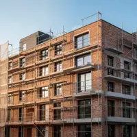 Ein Rohbau eines modernen Wohngebäudes mit Baugerüsten vor einem klaren blauen Himmel. - Foto: über boerse-global.de