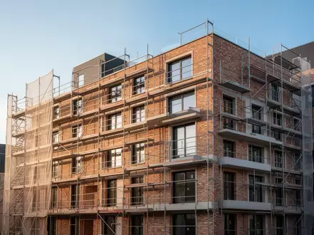 Ein Rohbau eines modernen Wohngebäudes mit Baugerüsten vor einem klaren blauen Himmel. - Foto: über boerse-global.de