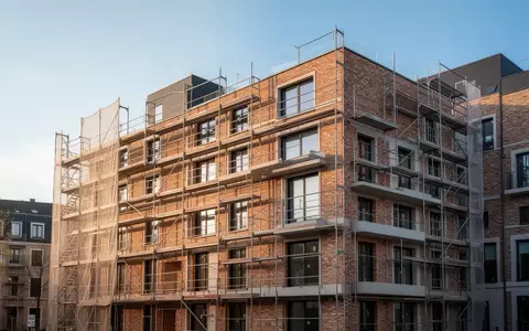 Ein Rohbau eines modernen Wohngebäudes mit Baugerüsten vor einem klaren blauen Himmel. - Foto: über boerse-global.de