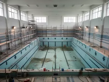 Leeres, sanierungsbedürftiges kommunales Schwimmbecken mit Gerüsten in einer Schwimmhalle ohne Personen. - Foto: über boerse-global.de