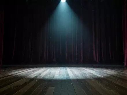 Eine leere, stimmungsvoll beleuchtete Theaterbühne mit schweren Vorhängen und einem einzelnen Scheinwerferstrahl auf dem Boden. - Foto: über boerse-global.de