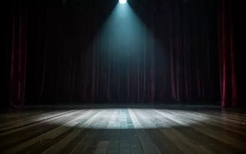 Eine leere, stimmungsvoll beleuchtete Theaterbühne mit schweren Vorhängen und einem einzelnen Scheinwerferstrahl auf dem Boden. - Foto: über boerse-global.de
