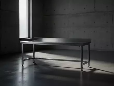 Ein minimalistischer, leerer Arbeitsraum mit einem industriellen Metalltisch und scharfen Schattenwurf auf dem Boden. - Foto: über boerse-global.de