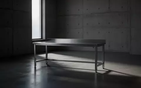 Ein minimalistischer, leerer Arbeitsraum mit einem industriellen Metalltisch und scharfen Schattenwurf auf dem Boden. - Foto: über boerse-global.de