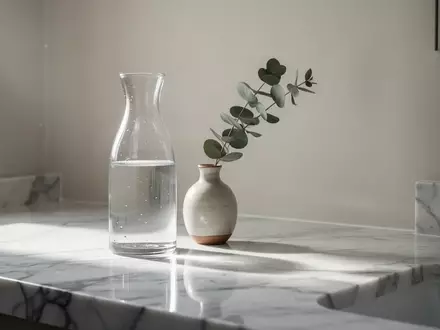 Ein minimalistisches, helles Badezimmer mit einer Marmoroberfläche, einer Glaskaraffe und einem Zweig Eukalyptus. - Foto: über boerse-global.de