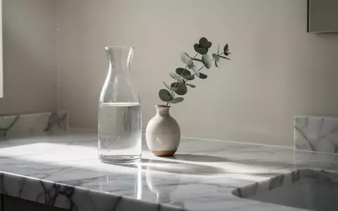 Ein minimalistisches, helles Badezimmer mit einer Marmoroberfläche, einer Glaskaraffe und einem Zweig Eukalyptus. - Foto: über boerse-global.de