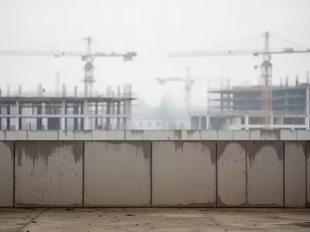 Eine leere Baustelle in Wien vor einem bewölkten Himmel mit Kränen im Hintergrund. - Foto: über boerse-global.de