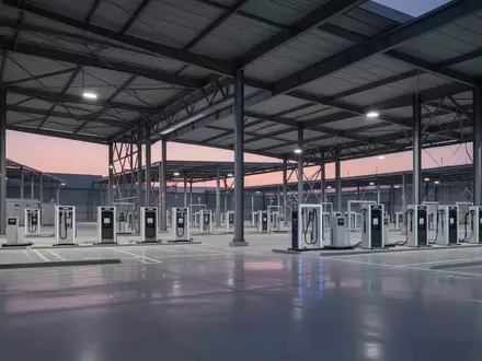 Eine weitläufige, moderne Logistikanlage in der Dämmerung mit modularen Batteriewechselstationen unter industriellen Vordächern. - Foto: über boerse-global.de