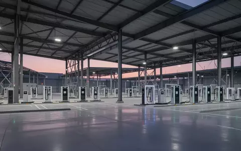 Eine weitläufige, moderne Logistikanlage in der Dämmerung mit modularen Batteriewechselstationen unter industriellen Vordächern. - Foto: über boerse-global.de