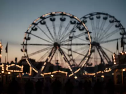 Blick auf die Lichter einer Kirmes in der Abenddämmerung als Symbol für öffentliche Veranstaltungen. - Foto: über boerse-global.de