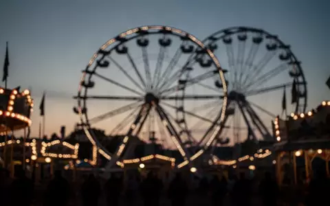 Blick auf die Lichter einer Kirmes in der Abenddämmerung als Symbol für öffentliche Veranstaltungen. - Foto: über boerse-global.de